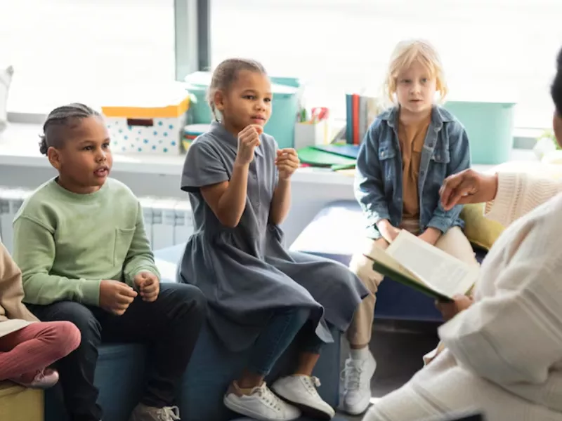 Diverse group of children listening to a teacher read, possibly related to managing a Language Disorder or Language Difference
